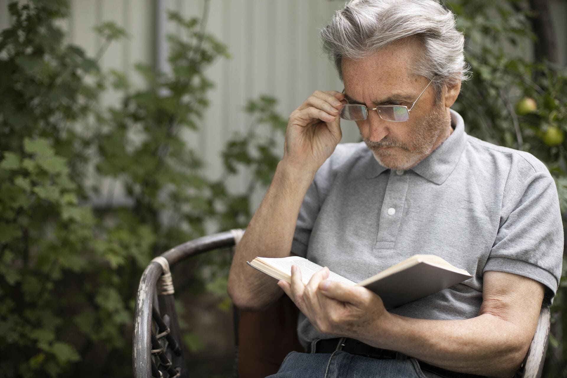 Homem idoso com óculos lendo, representando sintomas de presbiopia
